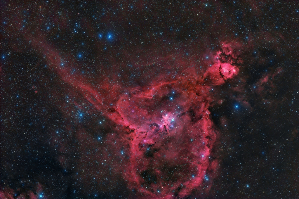 The “Heart Nebula” show the reddish glow of hydrogen atoms energized by bright stars that form inside this emission nebula. Lanes and patches of dark nebulae are also visible in the foreground of this star-forming region of the Milky Way.